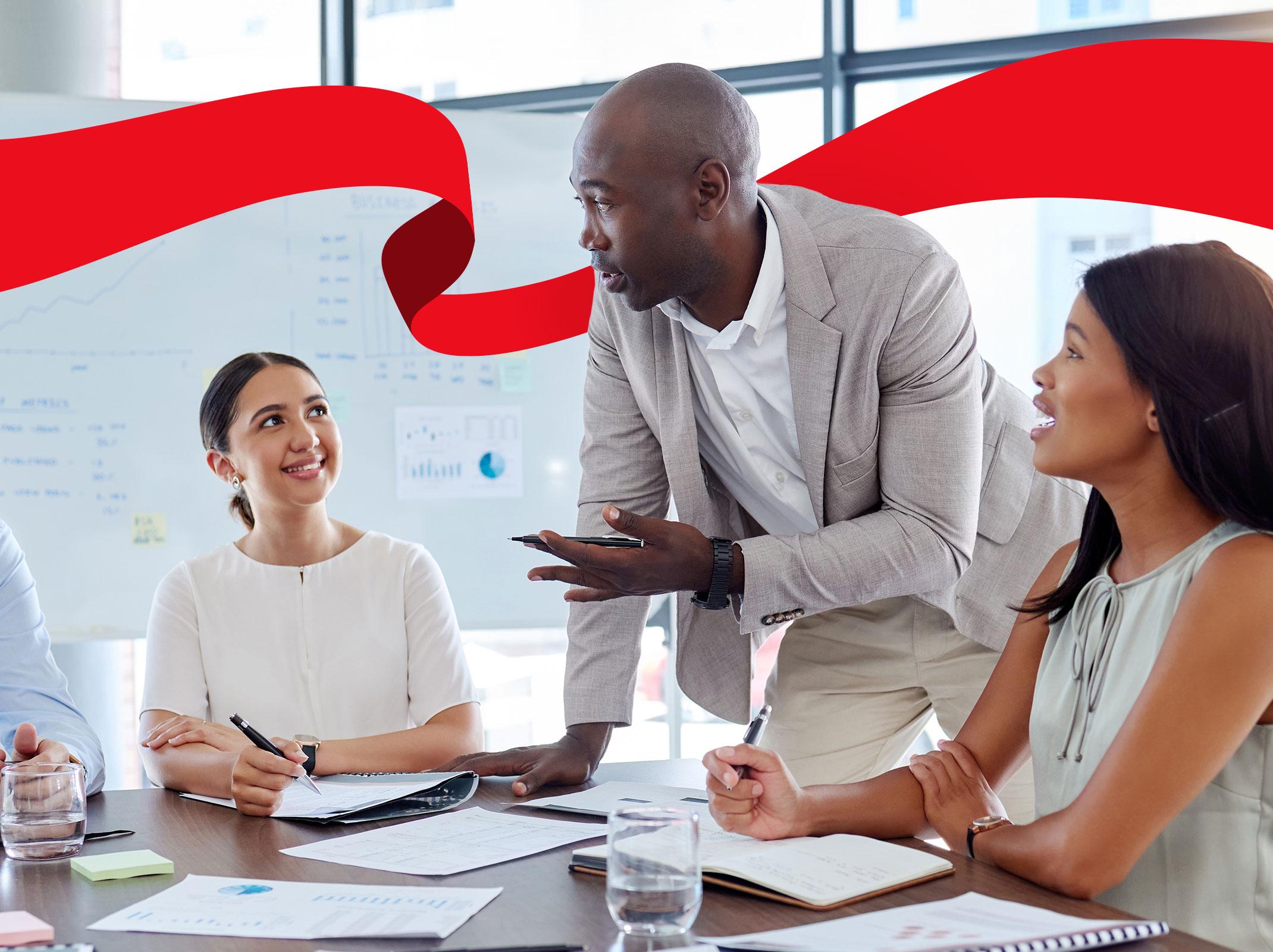 The image depicts a manager with two employees in a professional setting. The manager is holding a coaching session with their team in a modern office environment.