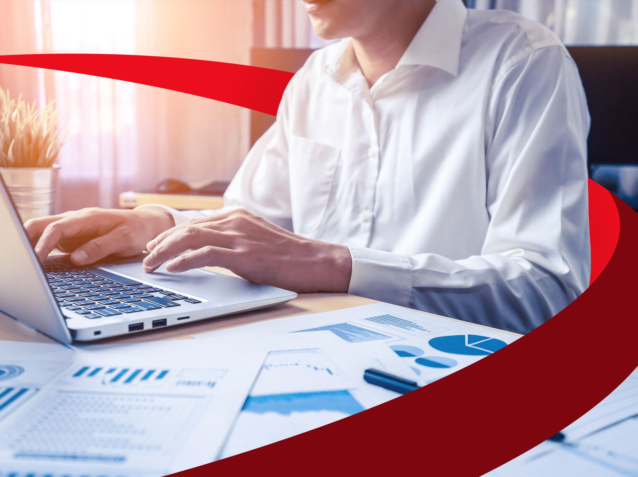 A business professional is seated in front of a laptop.  There are printouts of Microsoft Excel graphs and charts on her desk.