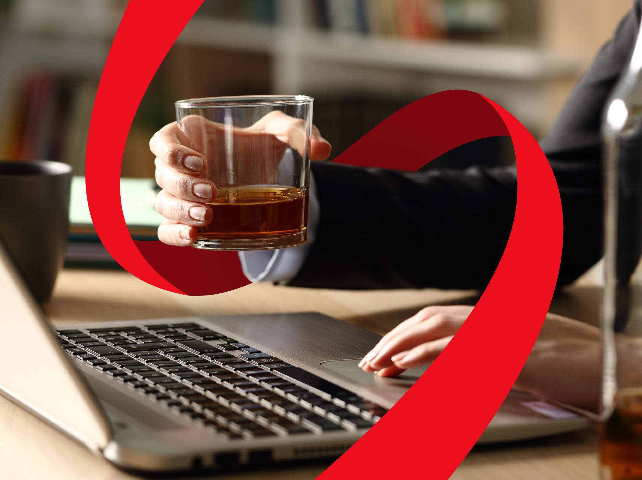 A business person working on a laptop with a drink in their hand.