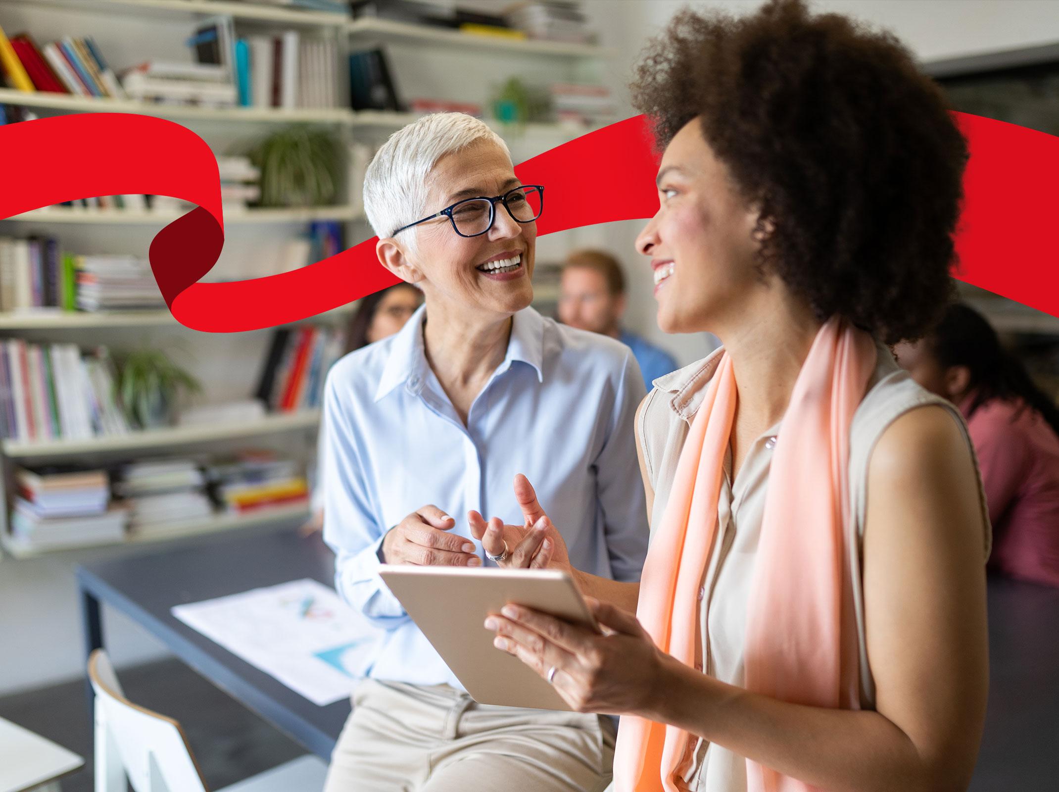 Two business professionals smiling at each other over a tablet in a business setting.