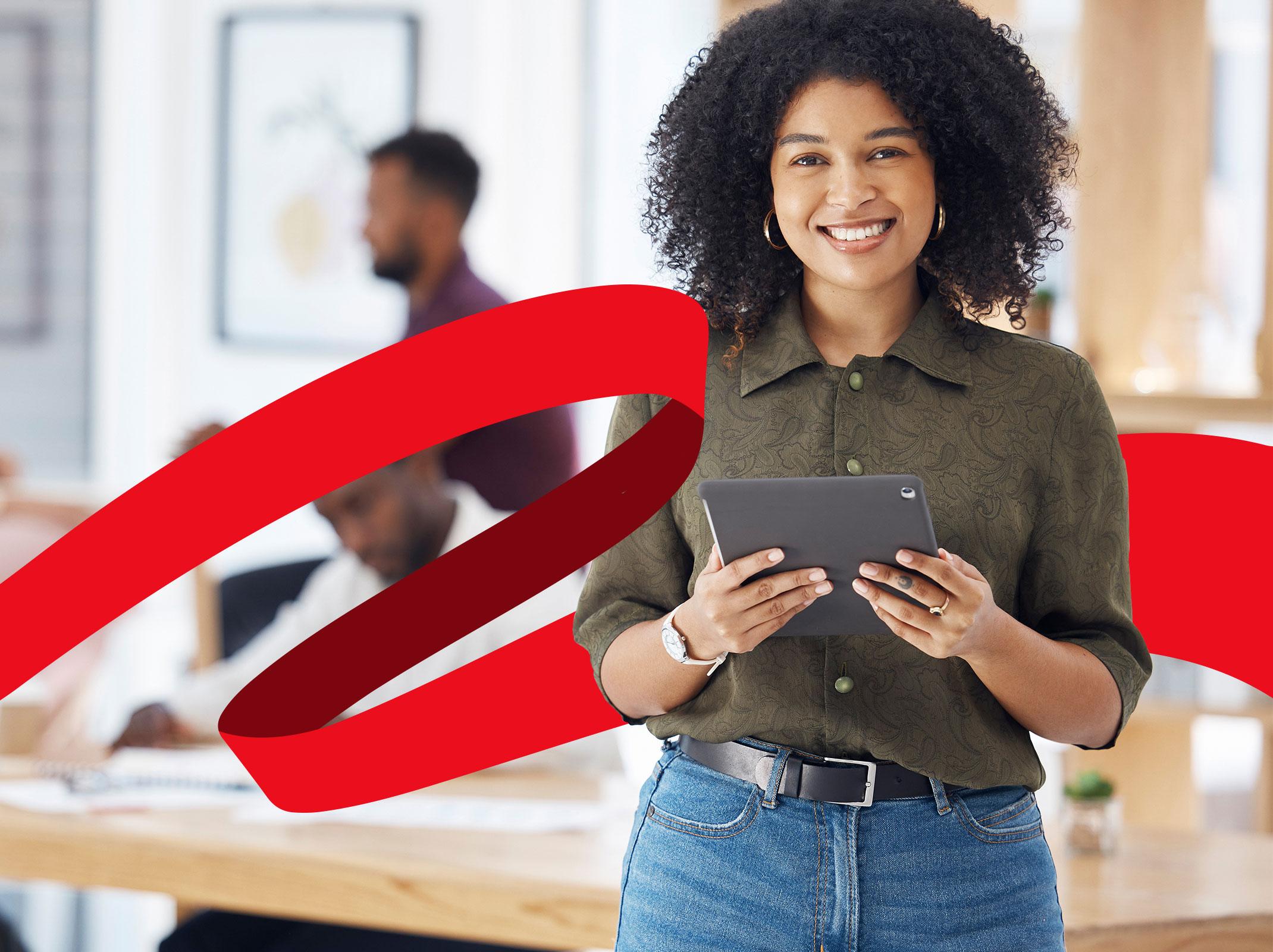Administrative professional in a business setting standing in front of a conference table holding a tablet and smiling.