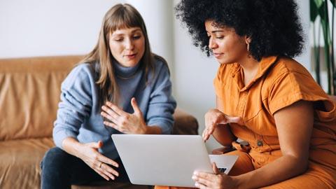 Female manager coaching a female employee over a laptop in an office setting.