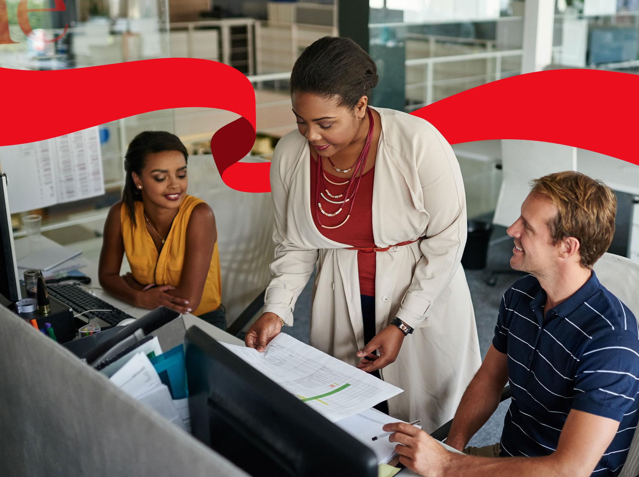 A business leader delegating items to two employees.  She is sharing a document in front of computer screens.