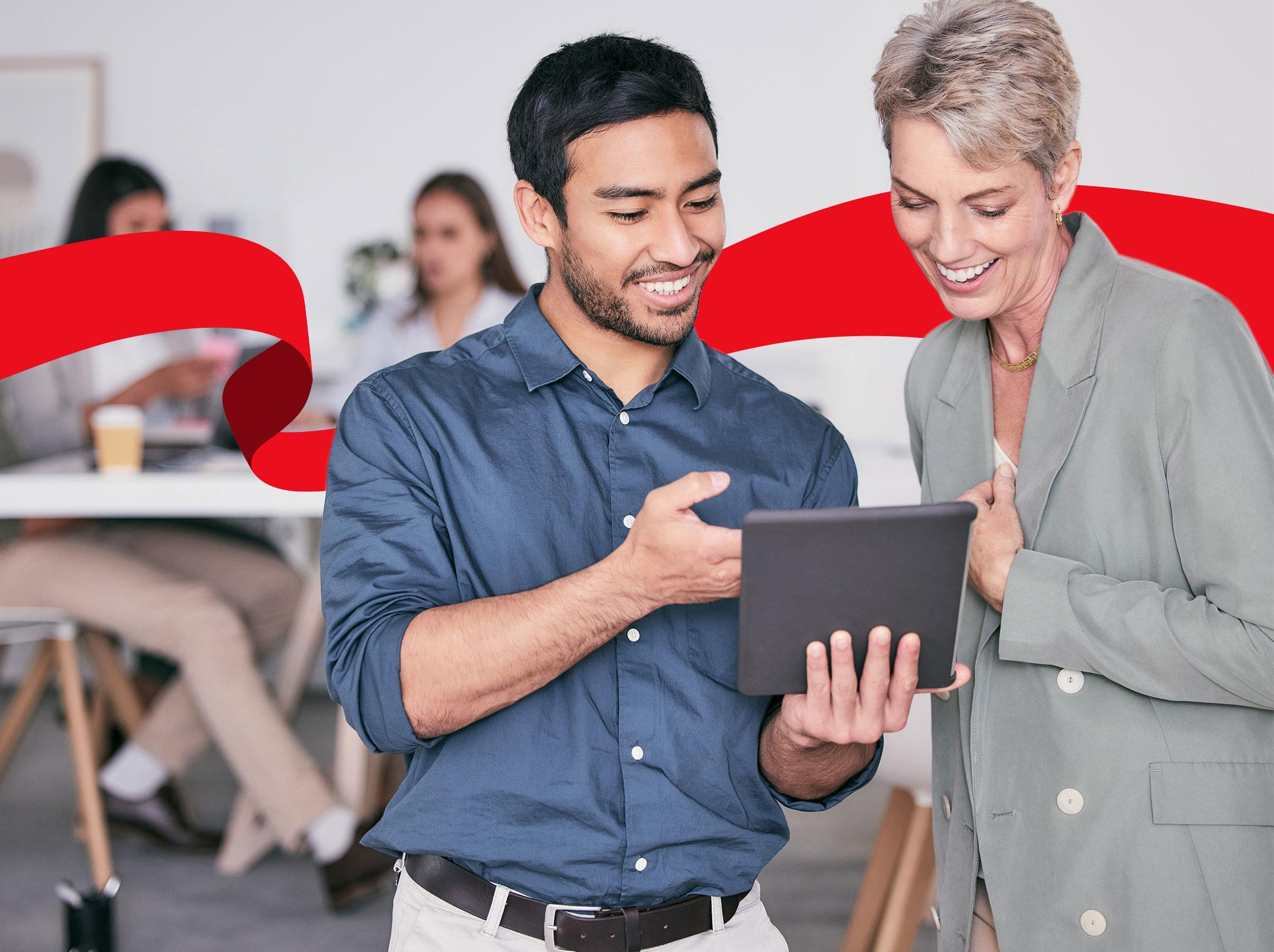 Human Resources professionals communicating with each other over a tablet with other coworkers in the background.