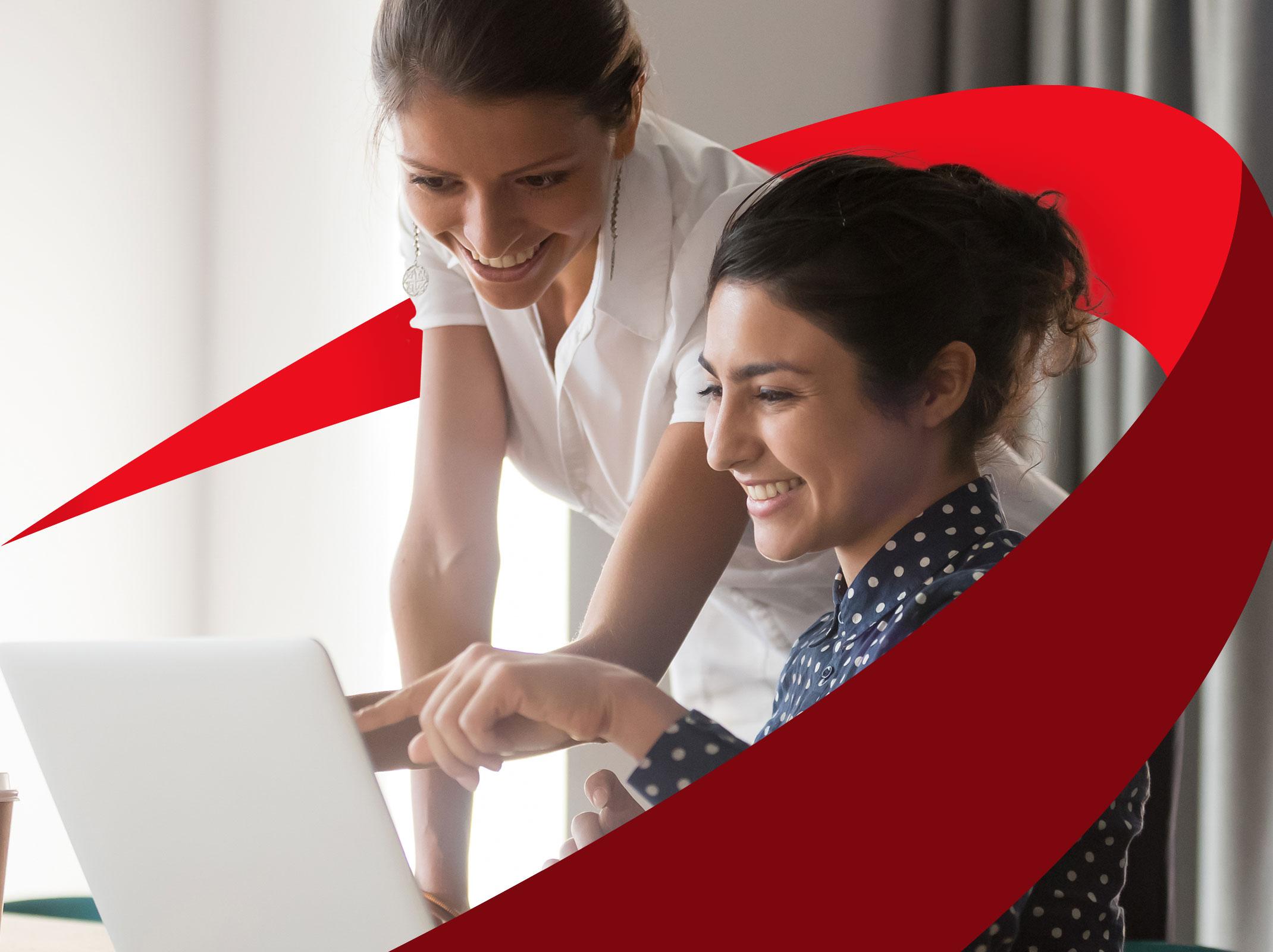 Two female business leaders reviewing something on a laptop.  One is pointing at the screen and both are smiling.