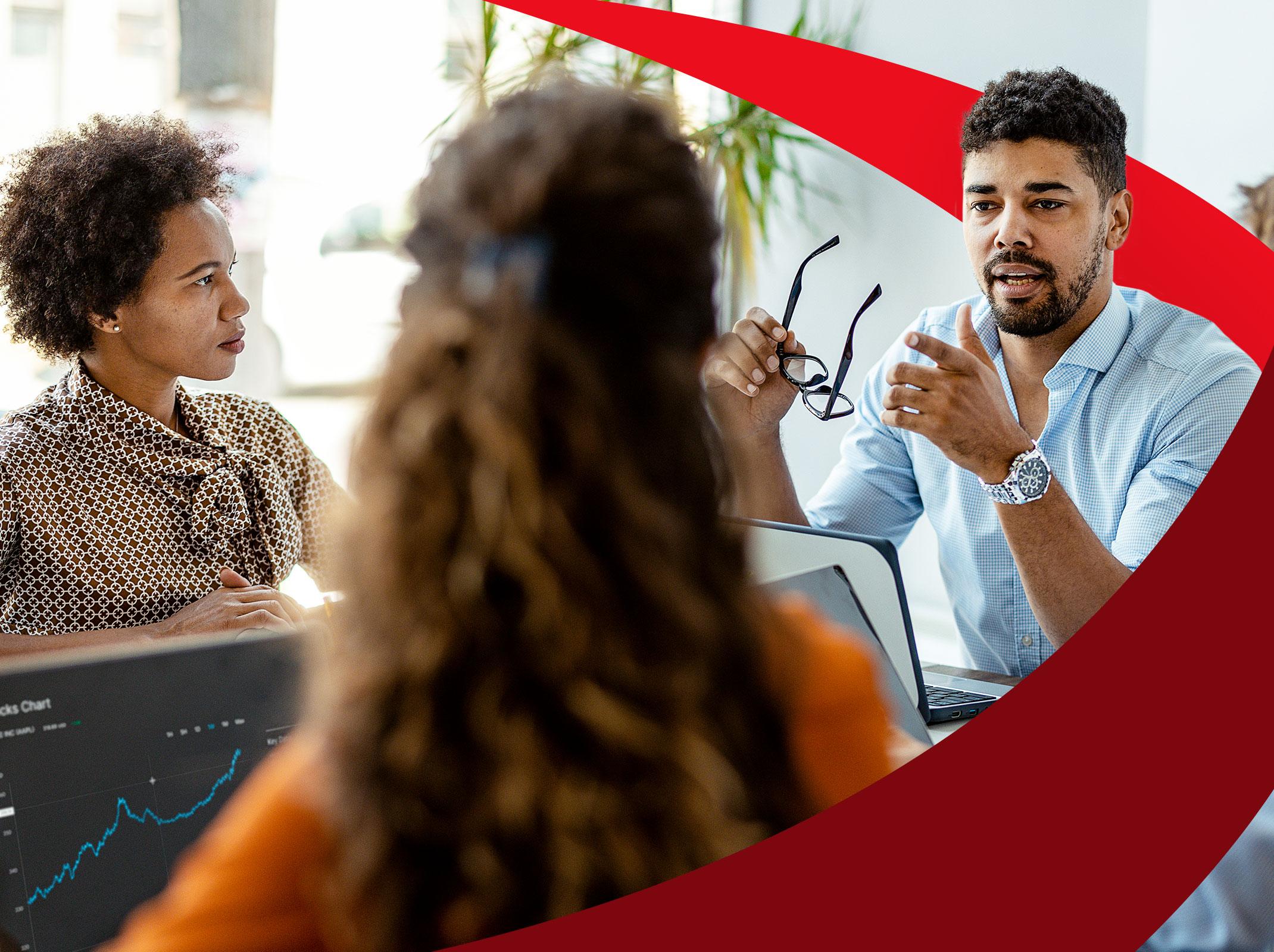 Man speaking to a group of colleagues around a conference table in a business setting.