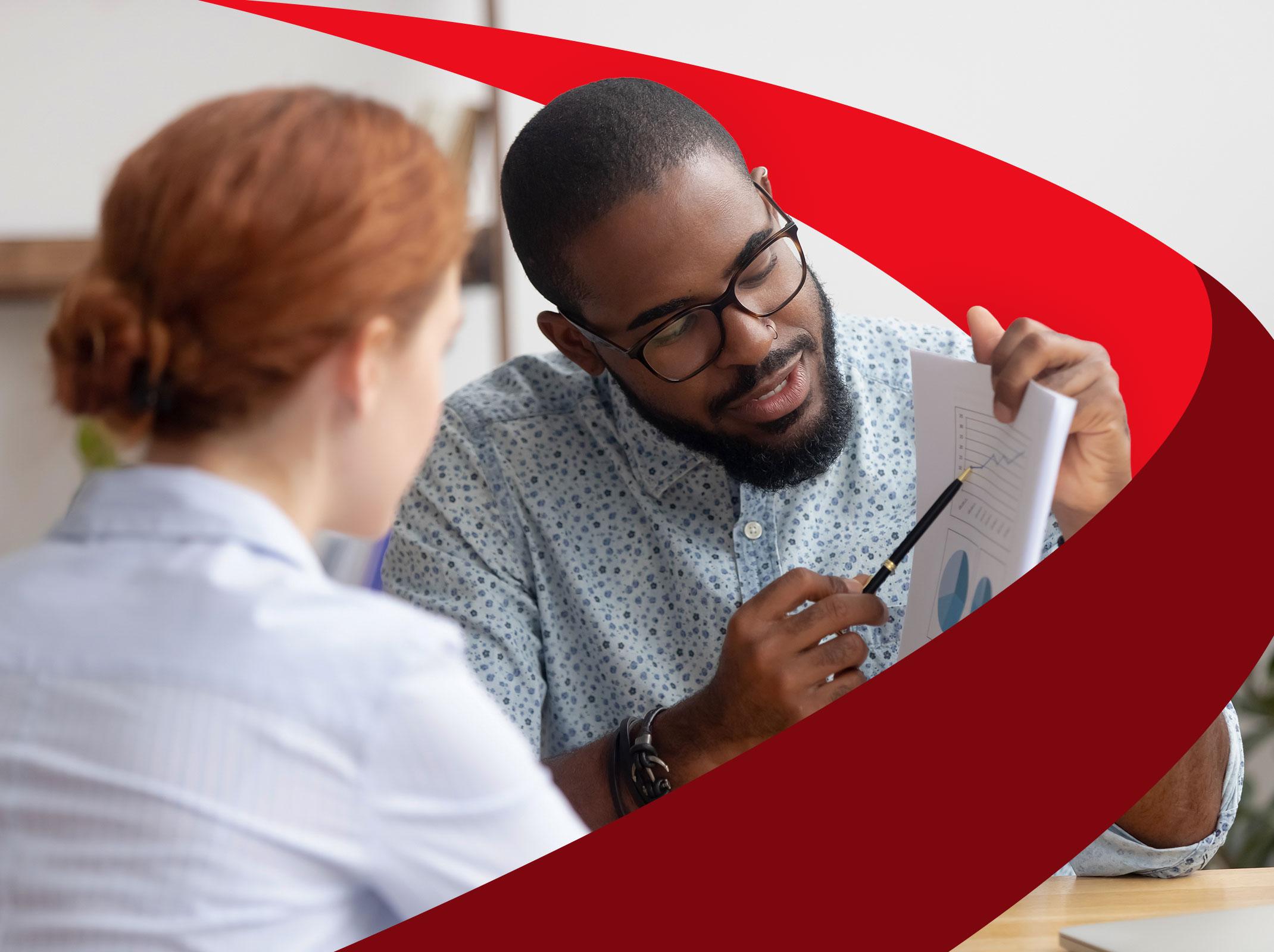 A leader mentoring an employee.  He is pointing at something on a piece of paper in a business setting.