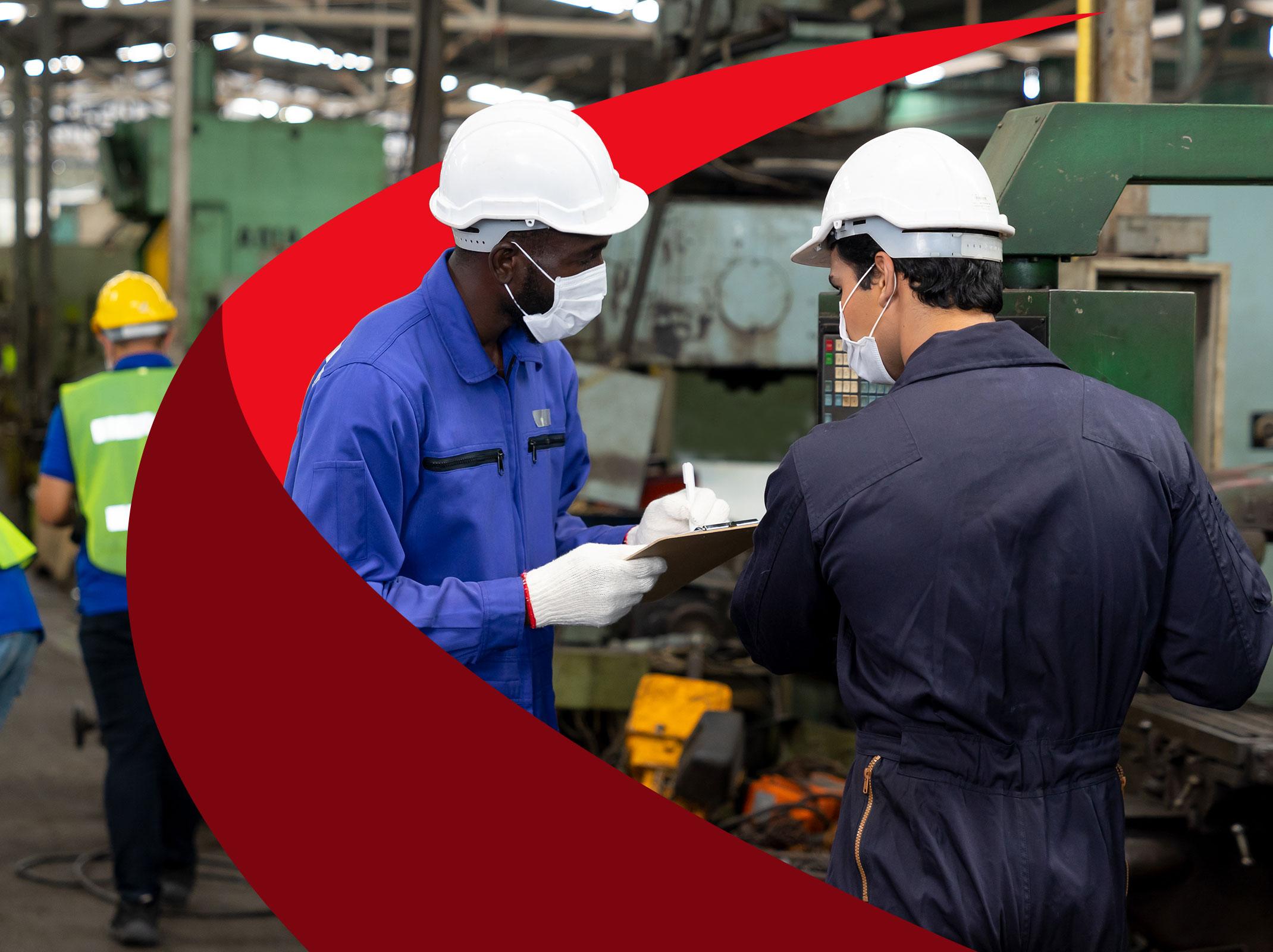 Workers in a manufacturing setting reviewing documents around machinery