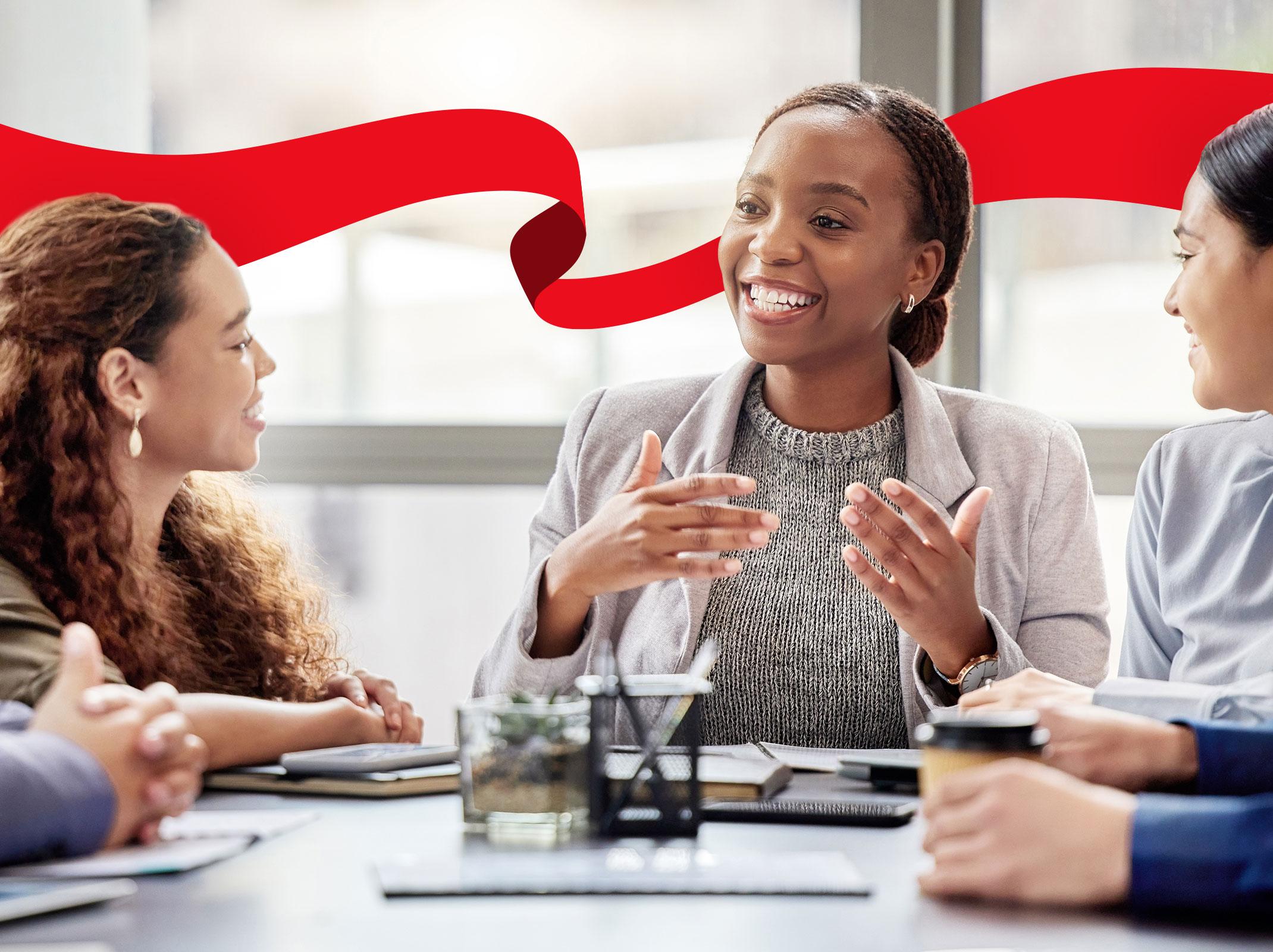 Several business professionals sitting around a conference table in an office setting.  One is speaking, smiling and gesturing with her hands.
