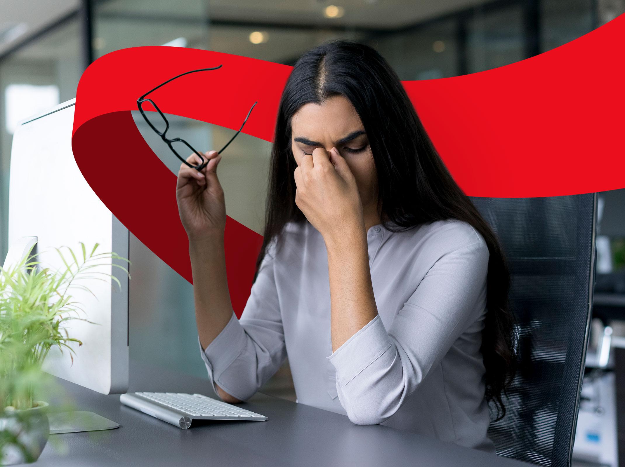 A female business professional with eyes closed pinching the bridge of her nose with her glasses in her other hand.  She appears to be stressed in a business setting.