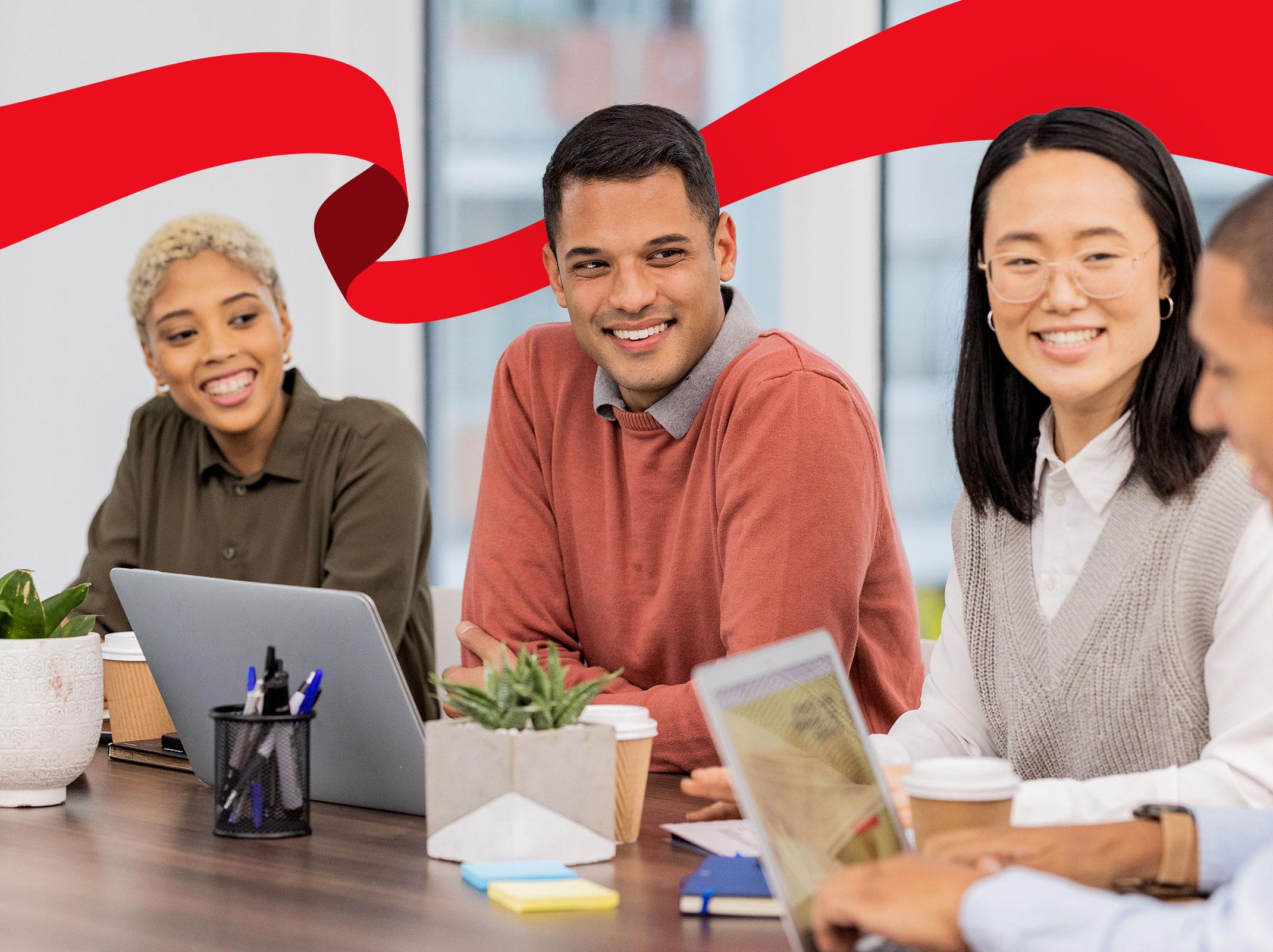 A group of professionals working at a table in an office setting.  They are smiling and interacting with one another.